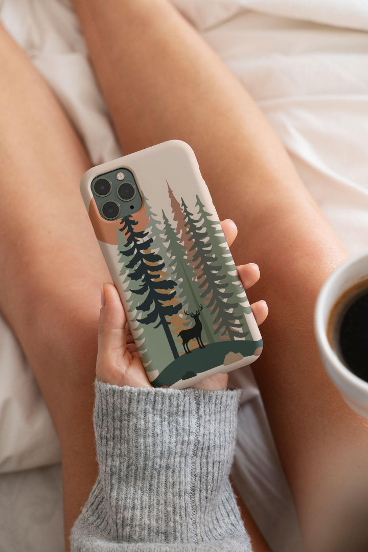 a woman holding a phone case with a forest scene on it